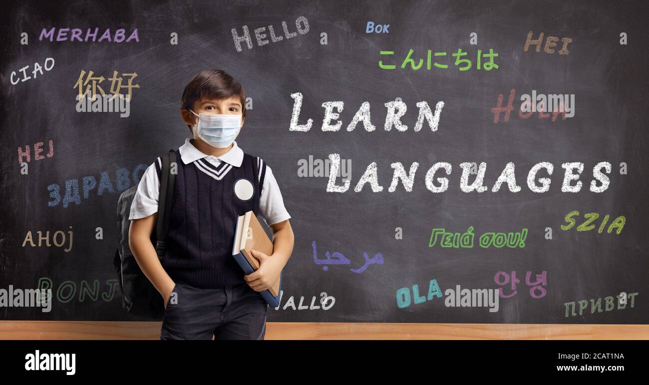 Schuljunge mit einer Schutzmaske vor einer Tafel mit Text Sprachen lernen Stockfoto