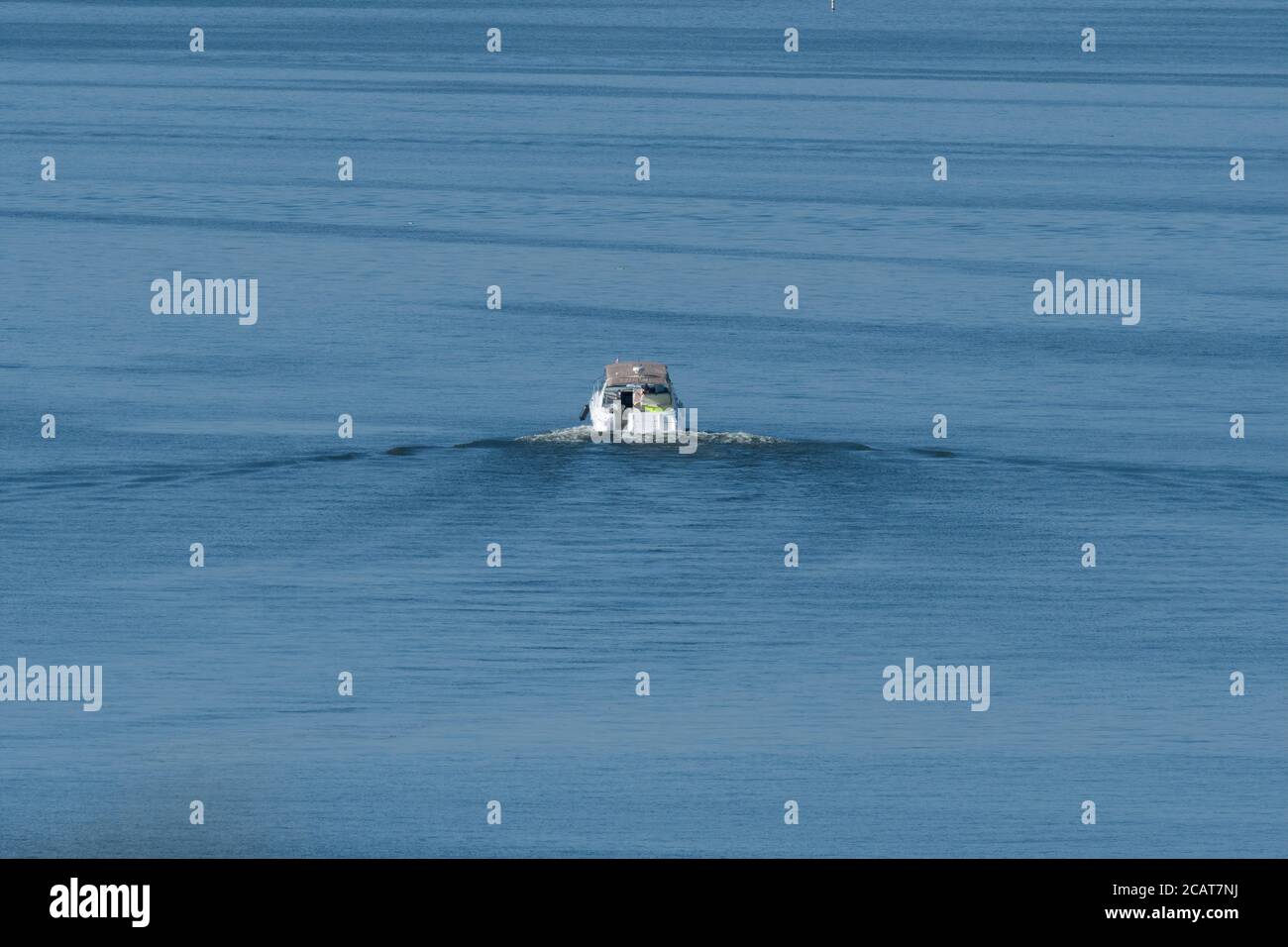 Ein Freizeitboot, das auf einem ruhigen blauen See unterwegs ist und hinter ihnen ein breites Wachen hinterlässt. Stockfoto