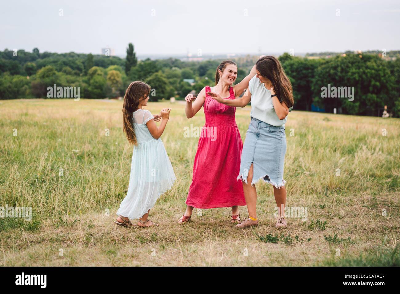 Drei Erwachsene kaukasische Schwestern spielen und haben Spaß auf dem Feld. Eine Familie von drei jungen Frauen lacht und verbringt die Sommerzeit in der Natur. Glücklich Stockfoto