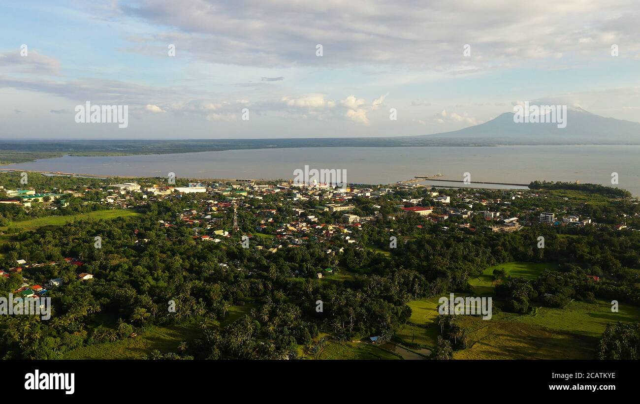 Blick auf eine kleine Stadt und einen Vulkan in der Ferne. Sorsogon City, Luzon, Philippinen. Asiatische Stadt am Meer, Blick von oben. Stockfoto
