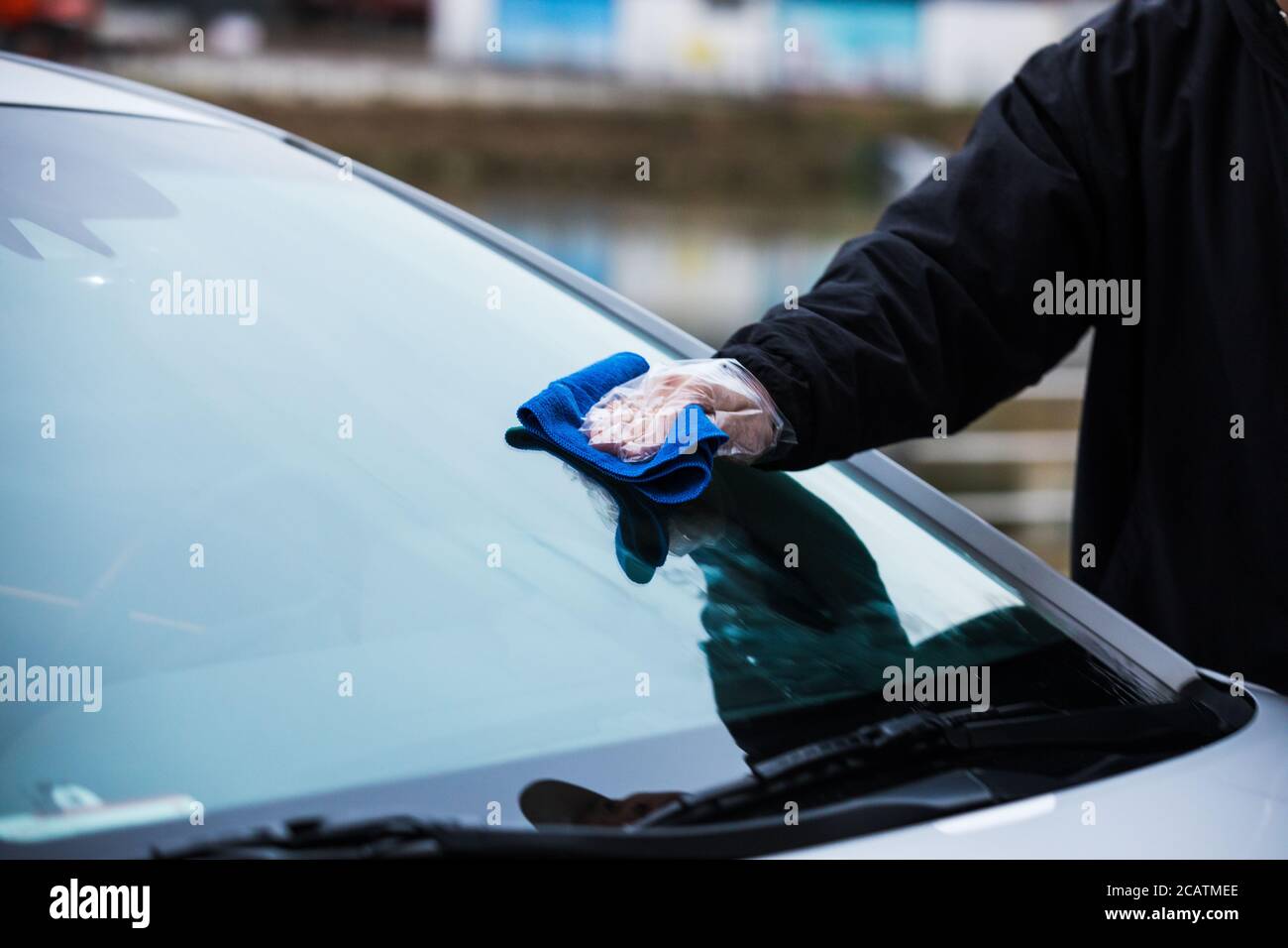 Die Windschutzscheibe eines Autos mit einem Mikrofasertuch von Hand reinigen Stockfoto