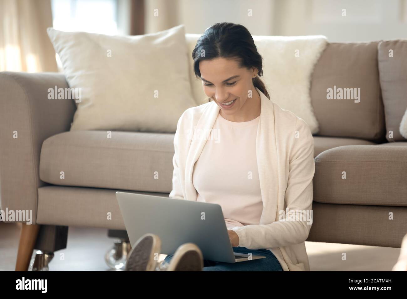 Lächelnde junge Frau, die auf dem Boden sitzt und den Computer benutzt. Stockfoto