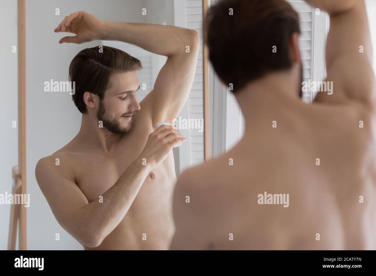 Spiegel Reflexion zufrieden jungen Mann Anwendung Antitranspirant auf Achselhöhle Stockfoto