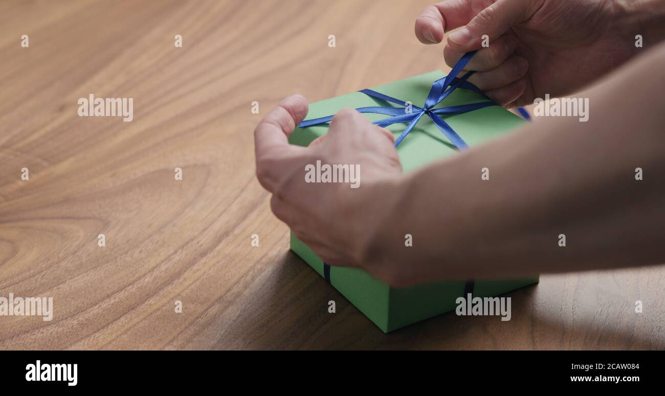 Mann Hand tyingblue Band auf grünem Papier Geschenkbox auf Tisch aus Nussbaum mit Platz zum Kopieren Stockfoto