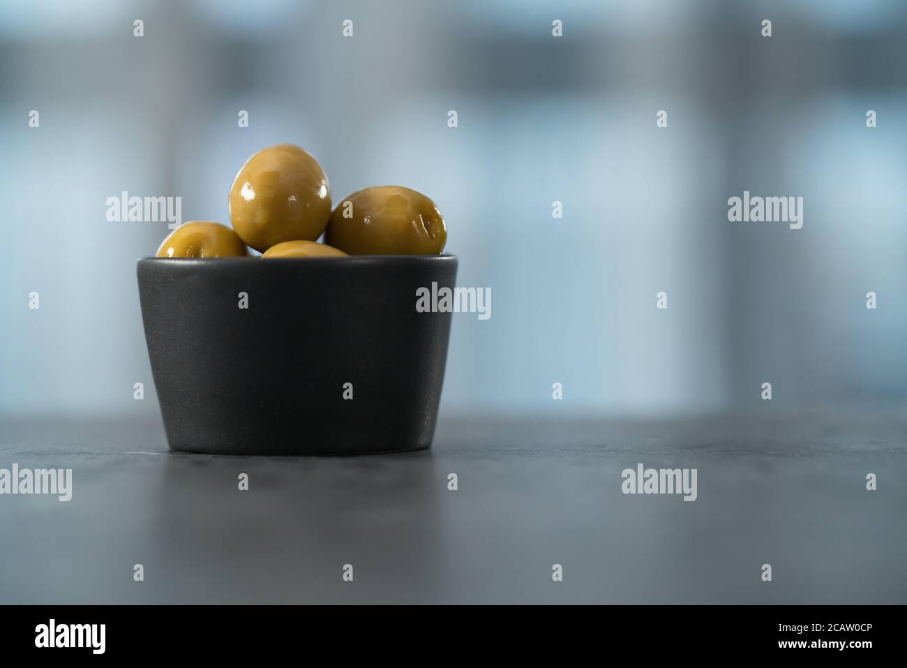 Ganze große grüne Oliven in kleiner schwarzer Schale auf Beton Hintergrund Stockfoto
