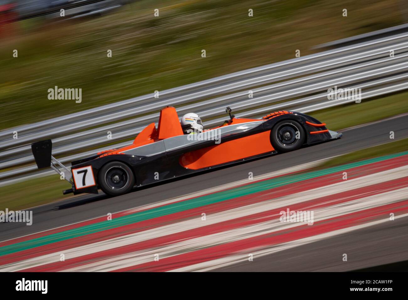 Eine Schwenkaufnahme eines schwarzen und orangen Rennwagens, der auf einer Rennstrecke fährt. Stockfoto