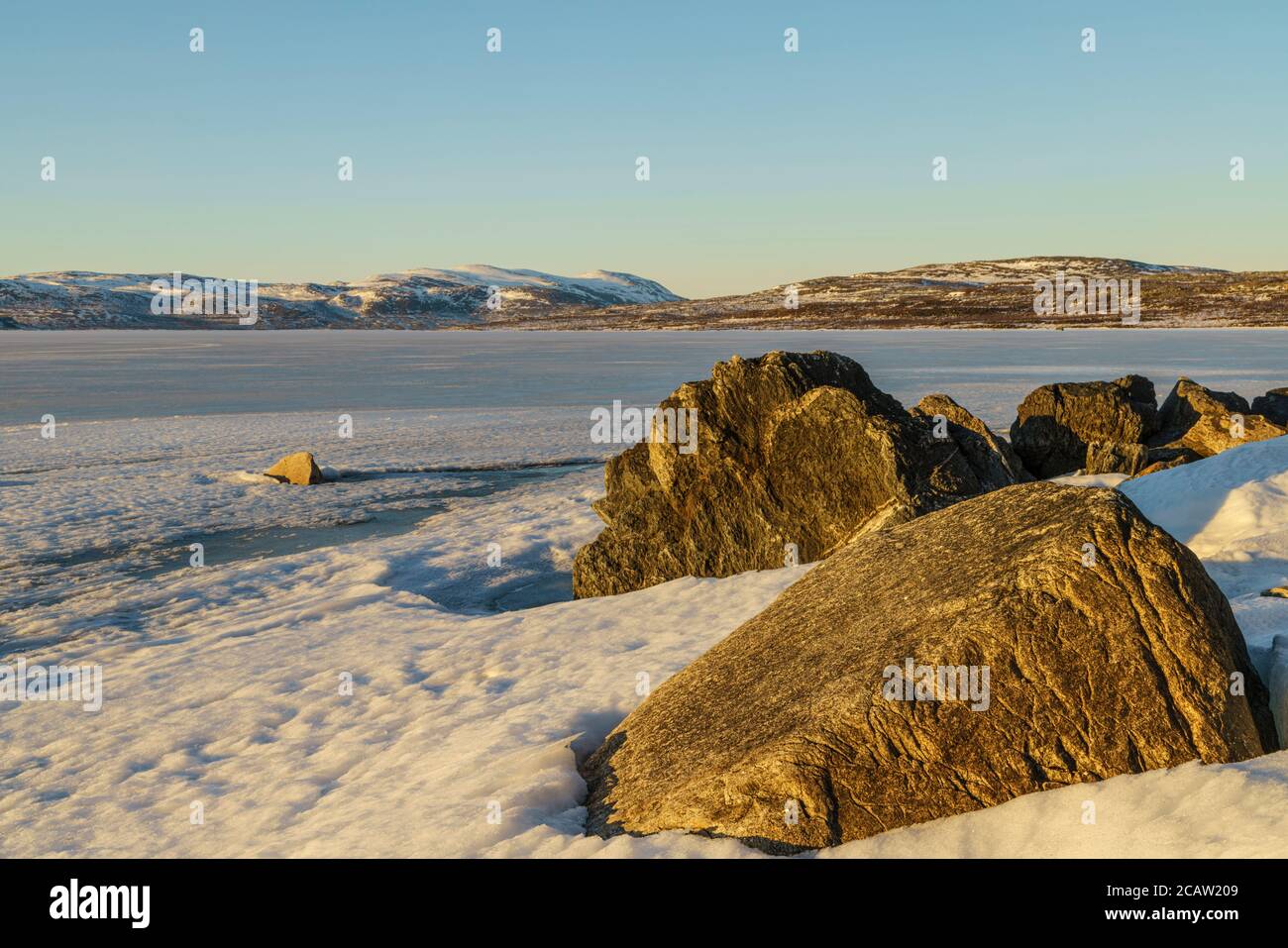 Schneelandschaft im Frühling mit Bergen im Hintergrund, gefrorener See Torneträsk, große Felsen im Vordergrund, Kiruna County, Schwedisch Lappland, Schweden Stockfoto