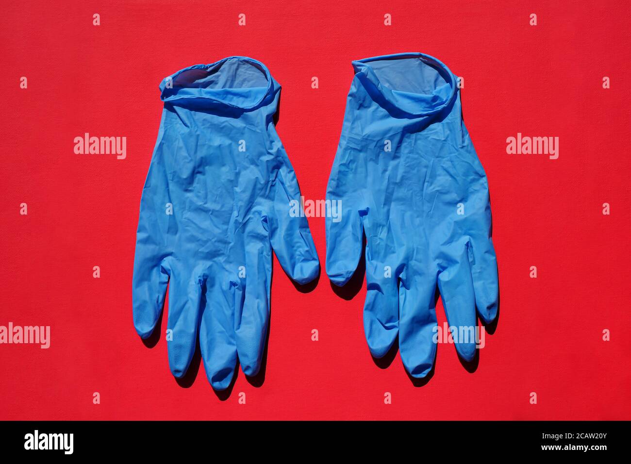 Paar medizinische blaue Latexschutzhandschuhe auf rotem Hintergrund. Schutzhandschuhe gegen die Ausbreitung von Virus, Grippe, Coronavirus (COVID-19). Stockfoto
