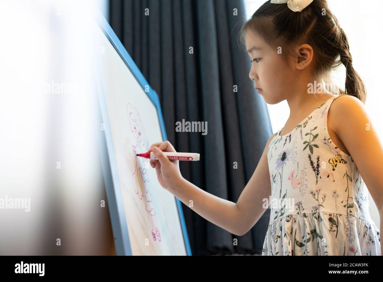 Asiatische Mädchen Grundschülerin Zeichnung auf Whiteboard zu Hause als Online-Aufgabe von der Schule, während Stadt Lockdown von COVID-19 Pandemie. Zuhause Schule Stockfoto