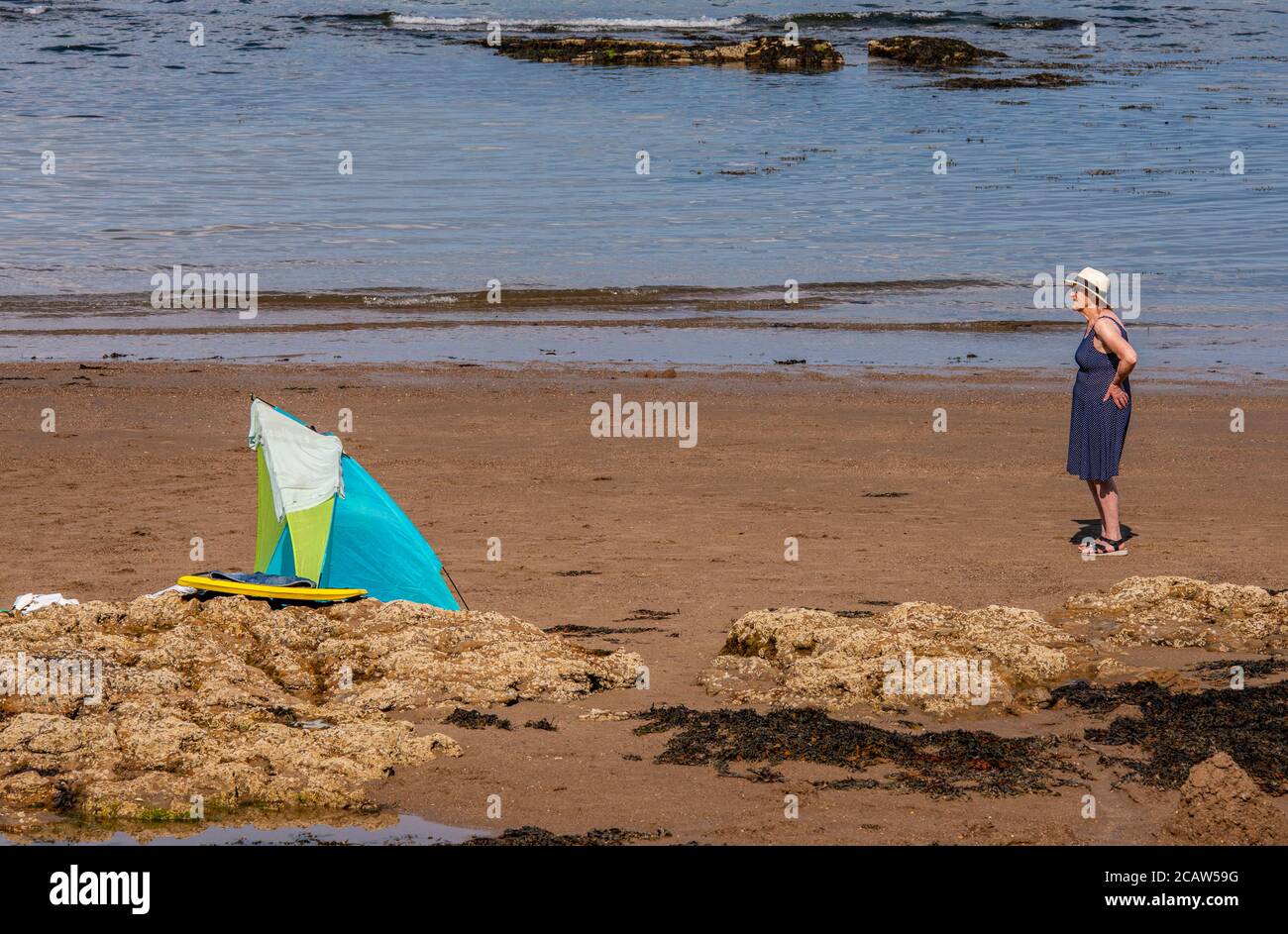 Eine Frau mit blauem Kleid und weißem Hut Blickt in die Ferne, während er in der Nähe eines Windschutzschalters steht Stockfoto