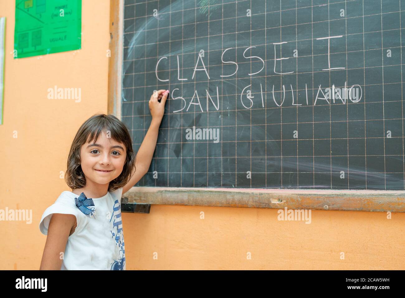 Junges Mädchen an ihrem ersten Tag der Grundschule im Klassenzimmer schriftlich auf der Tafel. Stockfoto