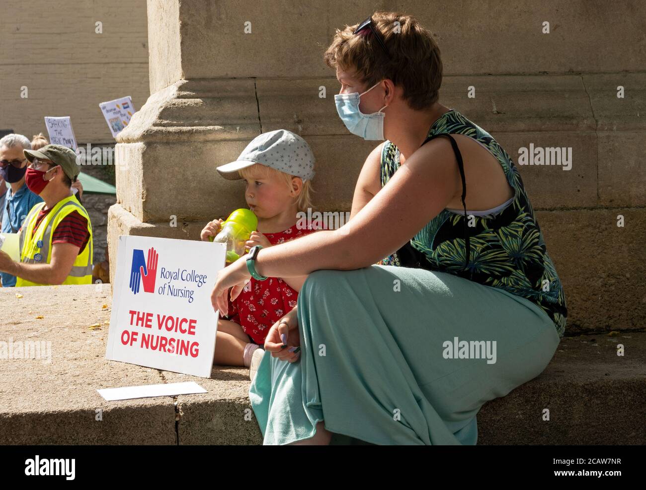 Oxford, Großbritannien. August 2020. NHS-Arbeiter und -Unterstützer nahmen an einer Kundgebung auf dem Bonner Platz in Oxford Teil, in der sie für Lohngerechtigkeit für alle NHS-Arbeiter aufriefen und protestierten, eine Lohnerhöhung zu fordern, um ihre Bemühungen während der covid Pandemie widerzuspiegeln.Dies war eine von etwa 38 ähnlichen Kundgebungen in ganz Großbritannien. Die Protestierenden behielten soziale Distanzierung aufrecht und trugen Masken. Während sie den Rednern zuhörten, hielten viele Plakate, die ihre Beschwerden und wie sie sich unterschätzt fühlten, hervorhoben. Frau und Kind halten RCN die Stimme der Krankenpflege Plakat. Quelle: Stephen Bell/Alamy Stockfoto