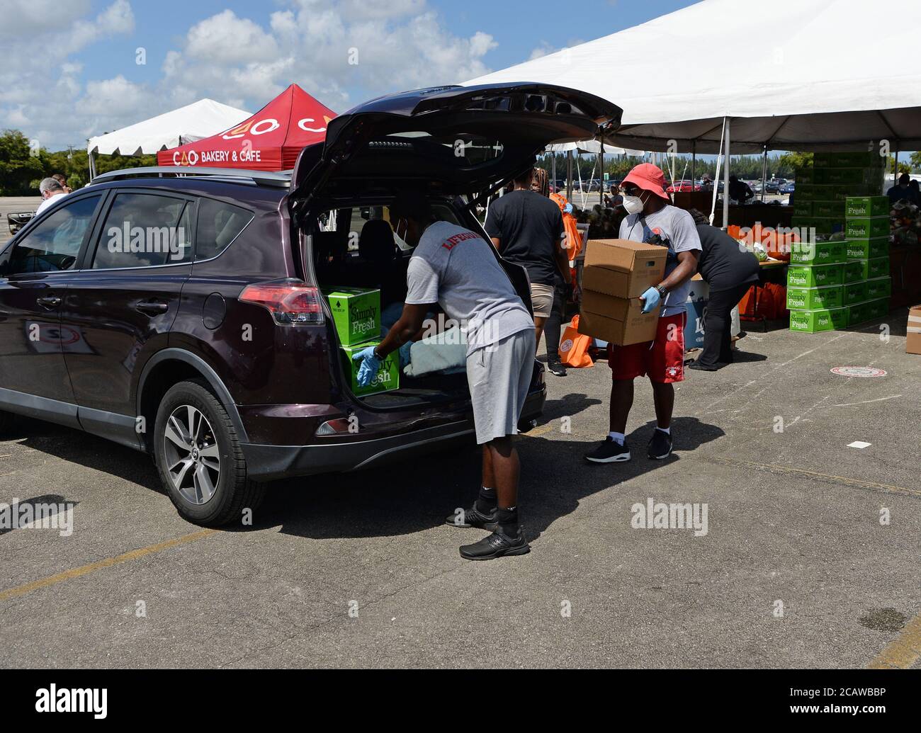 Miami Gardens Beach, FL, USA. August 2020. Freiwillige legen Lebensmittel in das Auto eines Empfängers während der Feed Your City Challenge im Calder Casino, gegründet vom Musikmogul Tony Draper und pensionierten NBA-Star Ricky Davis, Die landesweite Feed Your City Challenge Kampagne liefert frische Lebensmittel und persönliche Schutzausrüstung für benachteiligte Gemeinden, die von der Coronavirus (COVID-19) Pandemie betroffen sind. Am 8. August 2020 in Miami Gardens, Florida. Quelle: Mpi04/Media Punch/Alamy Live News Stockfoto