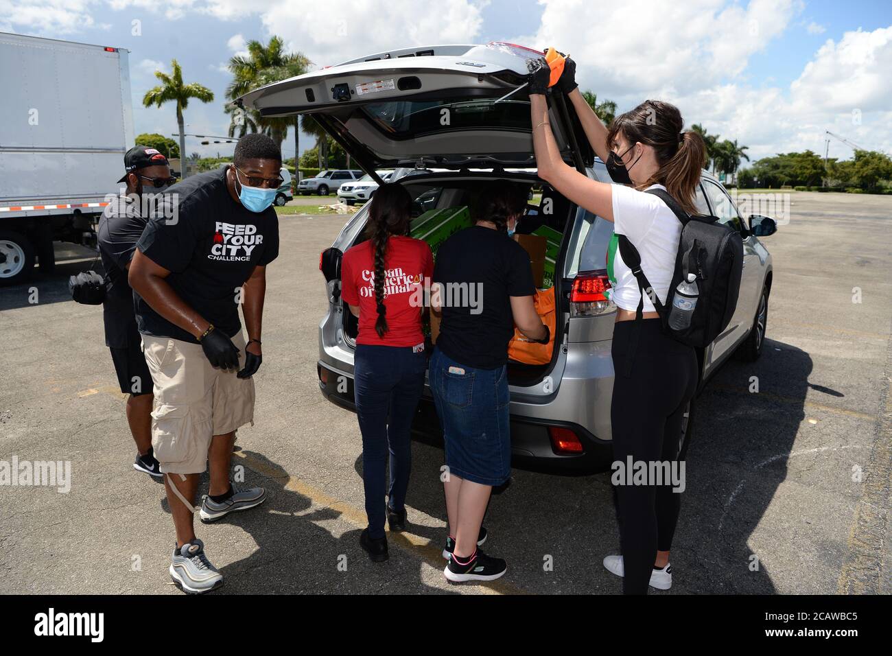 Miami Gardens Beach, FL, USA. August 2020. Freiwillige legen Lebensmittel in das Auto eines Empfängers während der Feed Your City Challenge im Calder Casino, gegründet vom Musikmogul Tony Draper und pensionierten NBA-Star Ricky Davis, Die landesweite Feed Your City Challenge Kampagne liefert frische Lebensmittel und persönliche Schutzausrüstung für benachteiligte Gemeinden, die von der Coronavirus (COVID-19) Pandemie betroffen sind. Am 8. August 2020 in Miami Gardens, Florida. Quelle: Mpi04/Media Punch/Alamy Live News Stockfoto