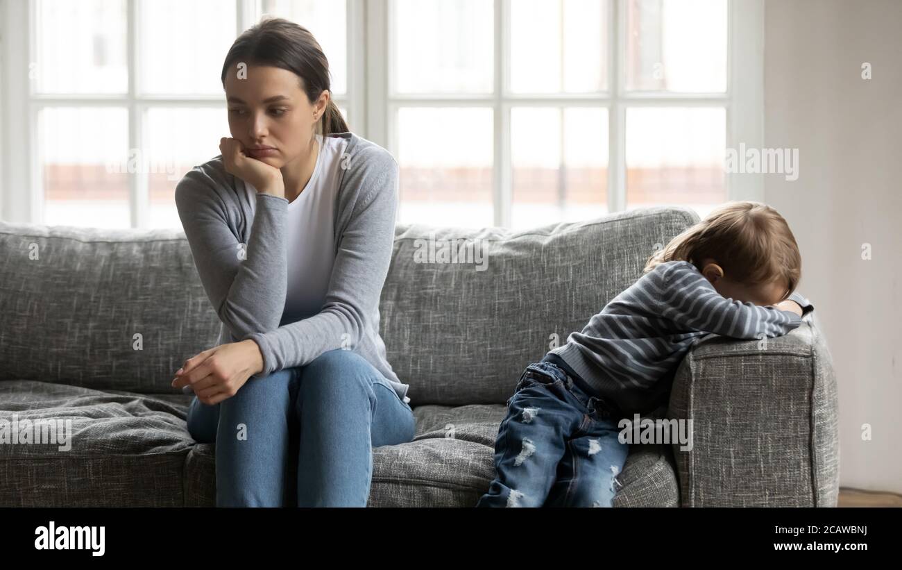 Gestresste junge Mama sitzt getrennt auf der Couch mit beleidigten Sohn. Stockfoto