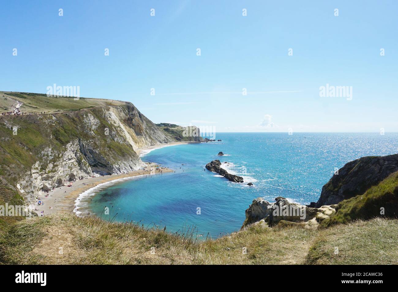 Sonnenanbeter genießen die Sonne im man o war Bay, Durdle Door mit seinen Sandstränden und dem ikonischen Kalksteinbogen, Lulworth Estate, Dorset, Großbritannien Stockfoto