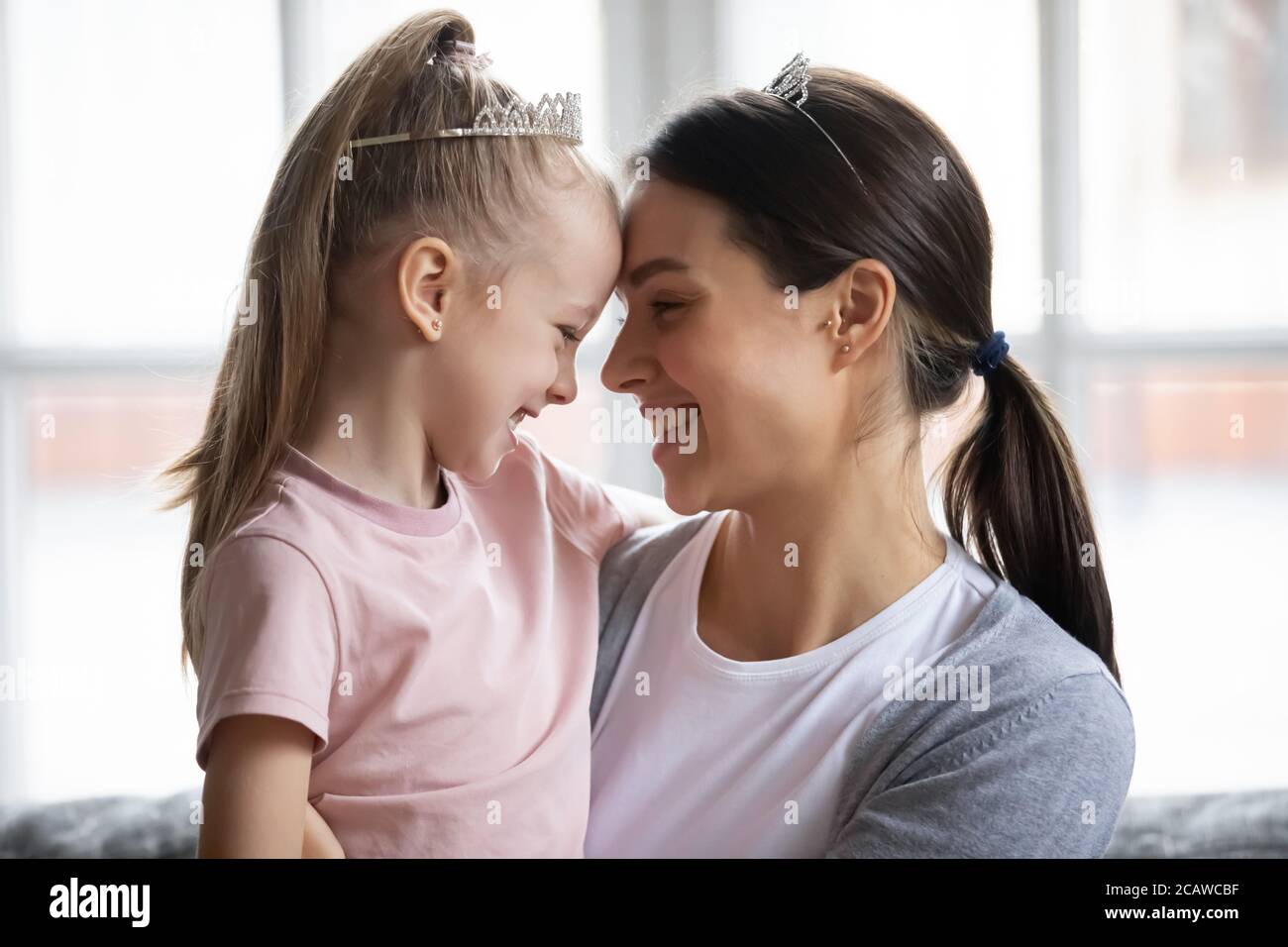 Happy Little blonde Mädchen berühren Stirn mit jungen Mutter. Stockfoto