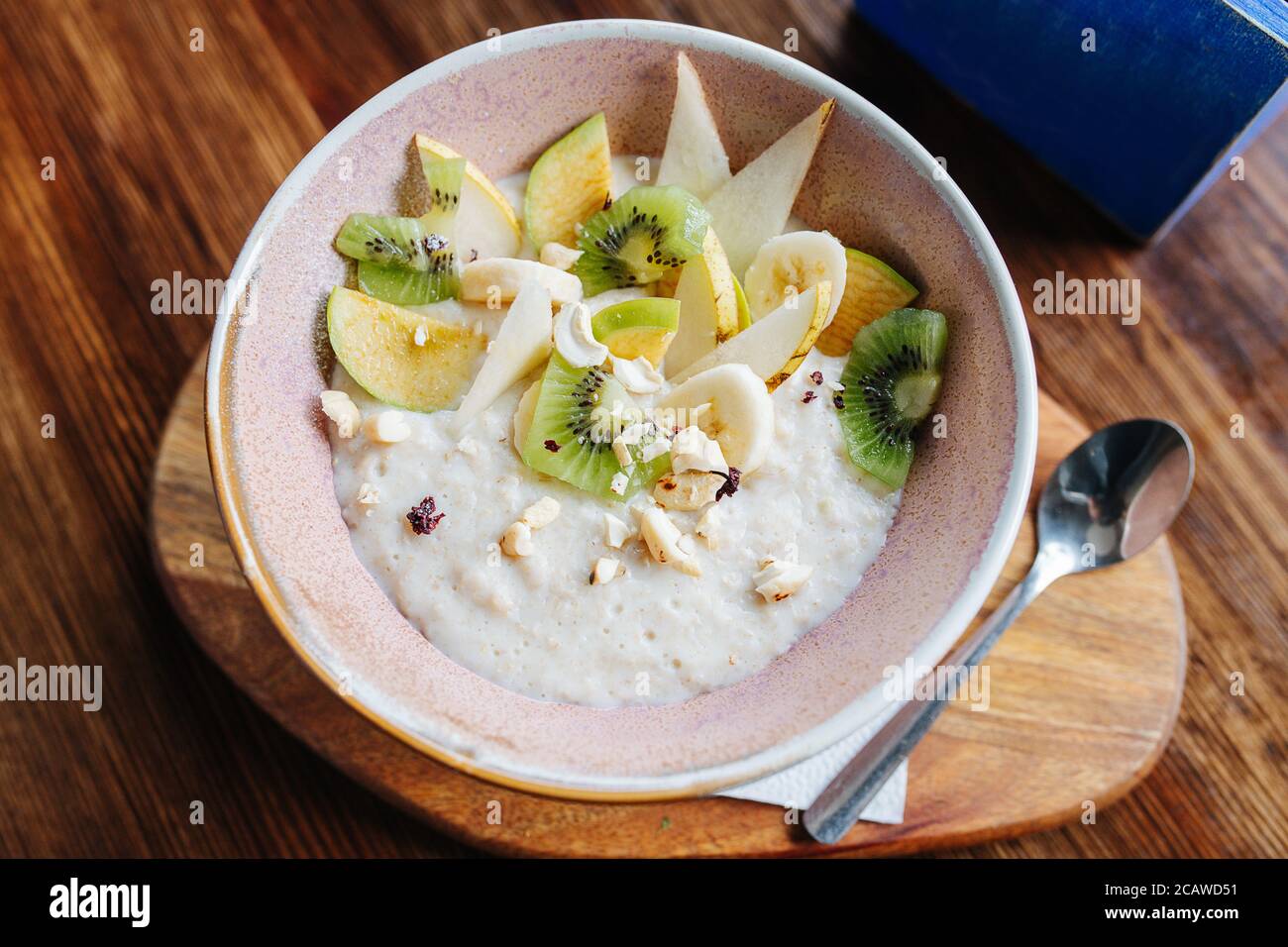 Haferflocken mit Früchten und Nüssen in einer Schüssel serviert Ein Brett mit einem Teelöffel Stockfoto