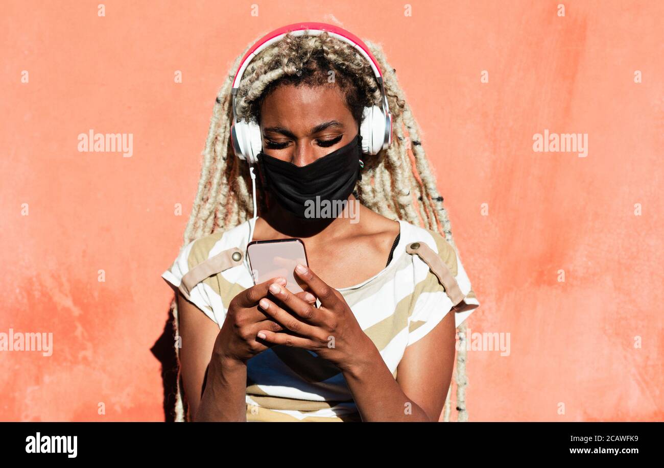 Junge afrikanische Frau mit Handy während der Wiedergabe Playlist Musik - Schwarze Mädchen tragen Gesichtsmaske für Coronavirus Prävention - Tech, Lifestyle und Stockfoto
