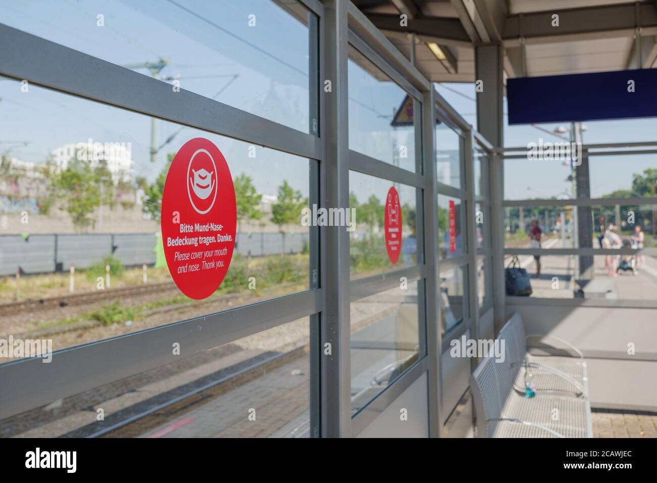 Warnschild des Passagiers: 'Bitte decken Sie Mund und Nase ab' auf der Glaswand am Bahnsteig-Bahnhof in Deutschland. Stockfoto