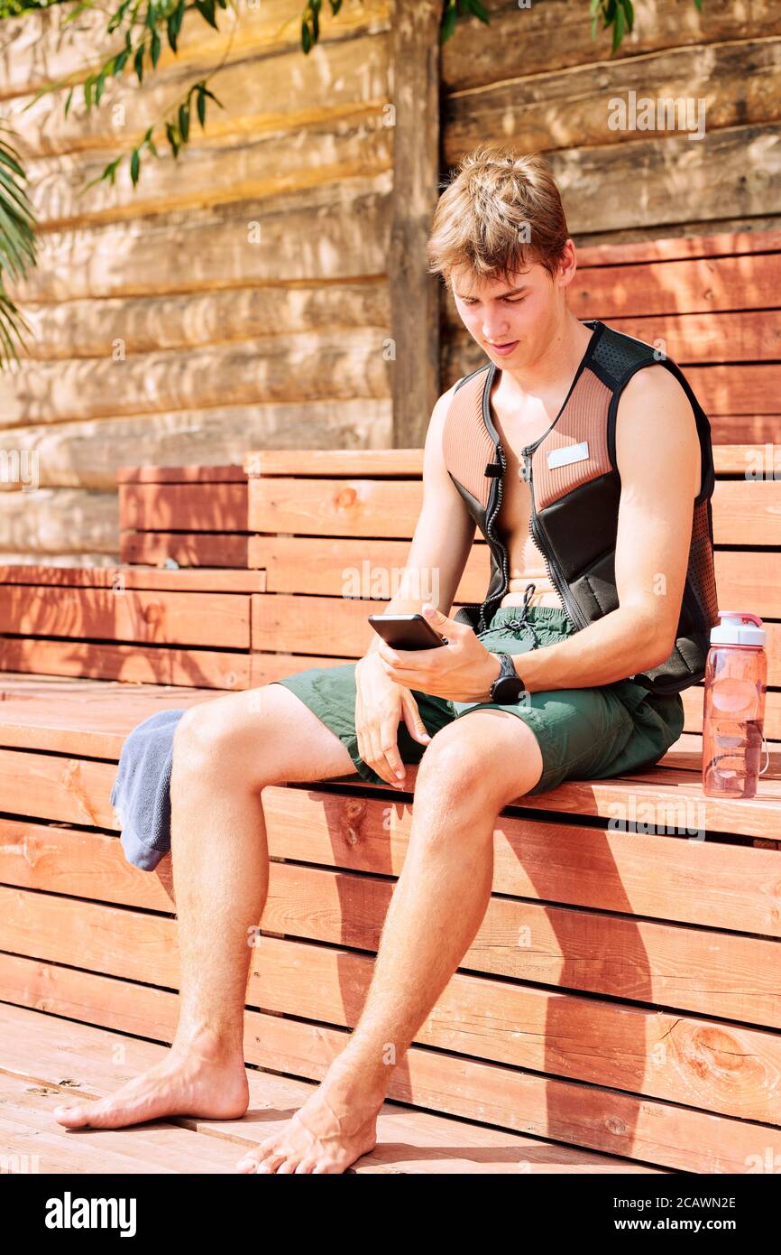 Zeitgemäßer Sportler in Shorts und Sicherheitsjacke Scrolling im Smartphone Stockfoto