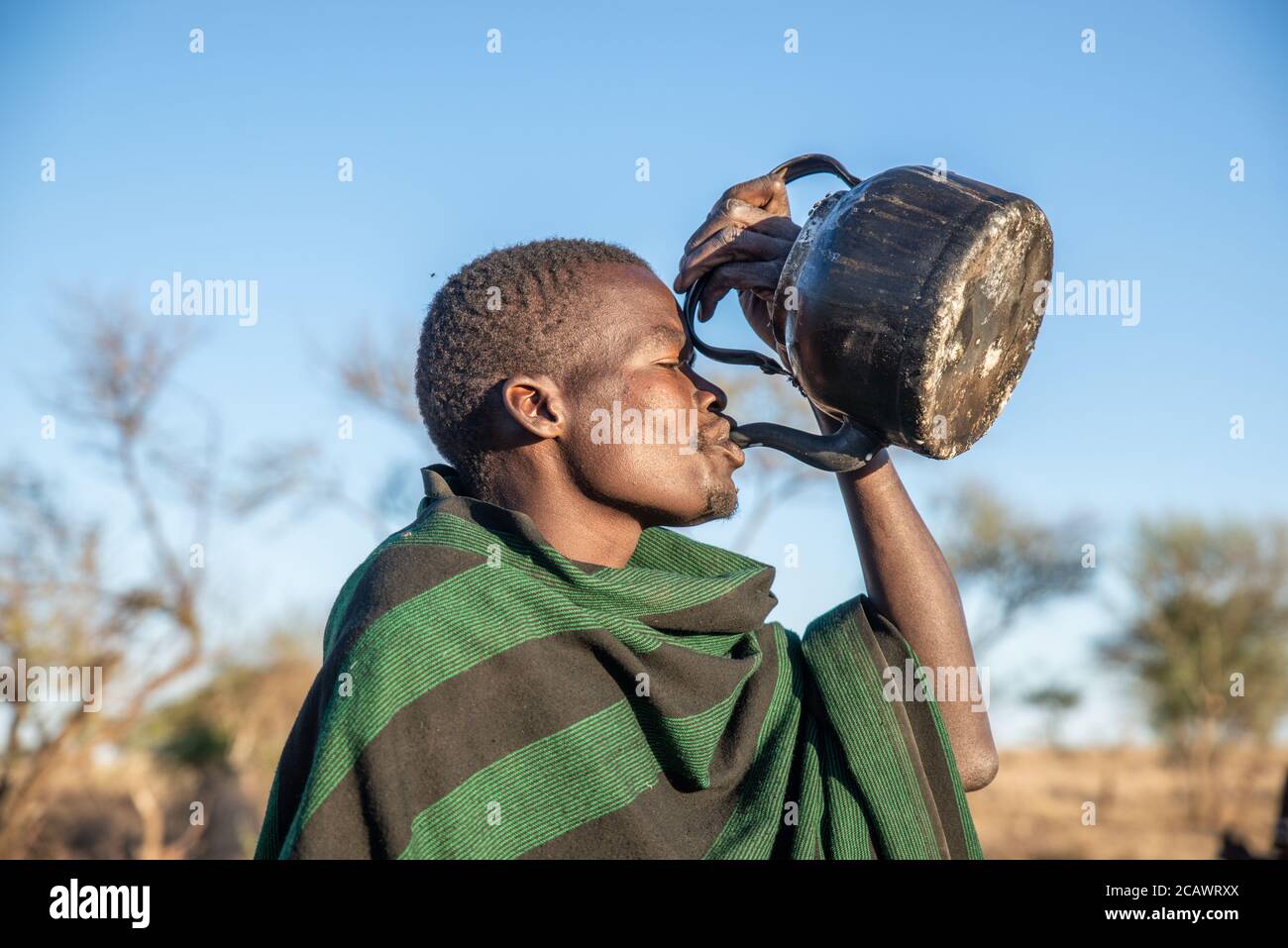 Karamojong Viehhirte mit traditionellen Decken trinken aus einem Wasserkocher, Moroto District, Uganda Stockfoto