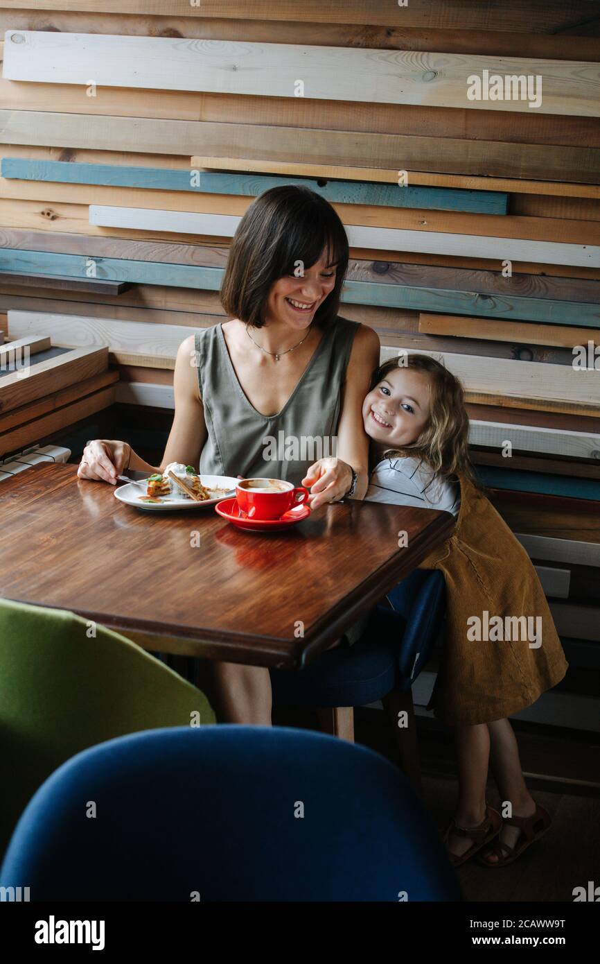 Glückliche Frau, die Kuchen in einem Café isst, während ihre Tochter ihre Zuneigung zeigt. Stockfoto