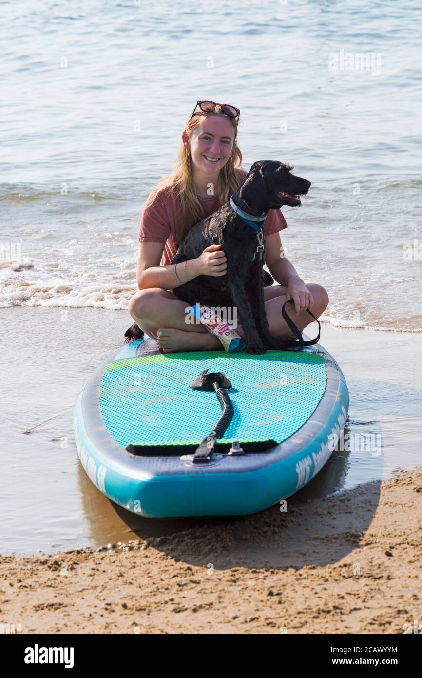 Junge Frau auf dem Paddleboard, Paddle Board, mit Kakadu Hund sitzt auf ihrem Schoß in Poole, Dorset, Großbritannien an heißen sonnigen Tag im August Stockfoto