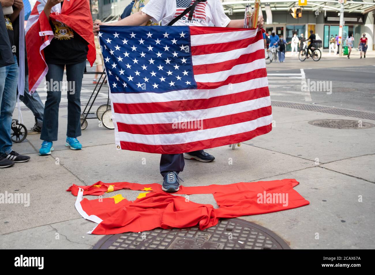 Ein Asiat hält eine amerikanische Flagge, als er auf eine zerrissene chinesische Flagge bei einem Protest gegen die Kommunistische Partei Chinas in Toronto, Ontario, tritt. Stockfoto