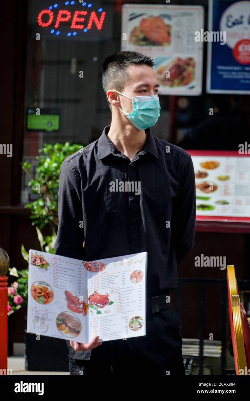 Mitarbeiter des chinesischen Restaurants in der Gerrard Street, Soho, London, mit einer chirurgischen Gesichtsmaske versucht, Kunden anzuziehen. Stockfoto