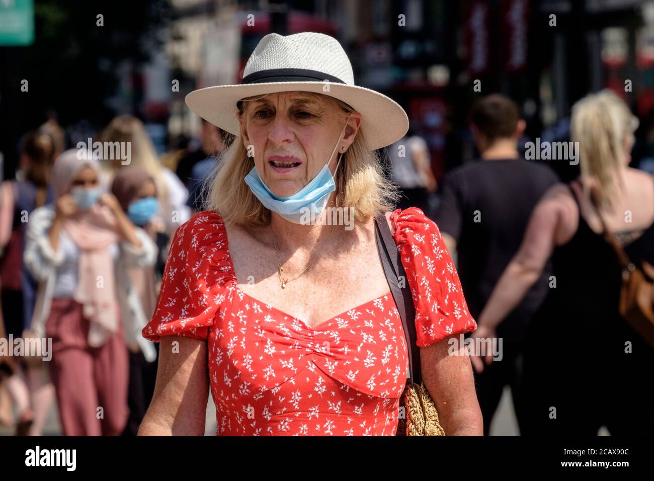 Eine Frau mittleren Alters, die Gesichtsbedeckung unter ihrem Kinn trägt, geht auf der geschäftigen Londoner Straße. Stockfoto