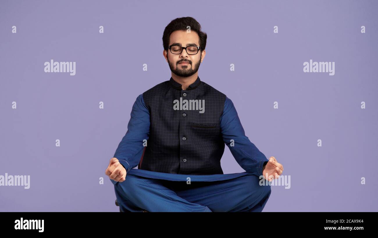 Stressmanagement. Ruhiger indischer Mann meditiert mit geschlossenen Augen über lilafarbischem Hintergrund Stockfoto