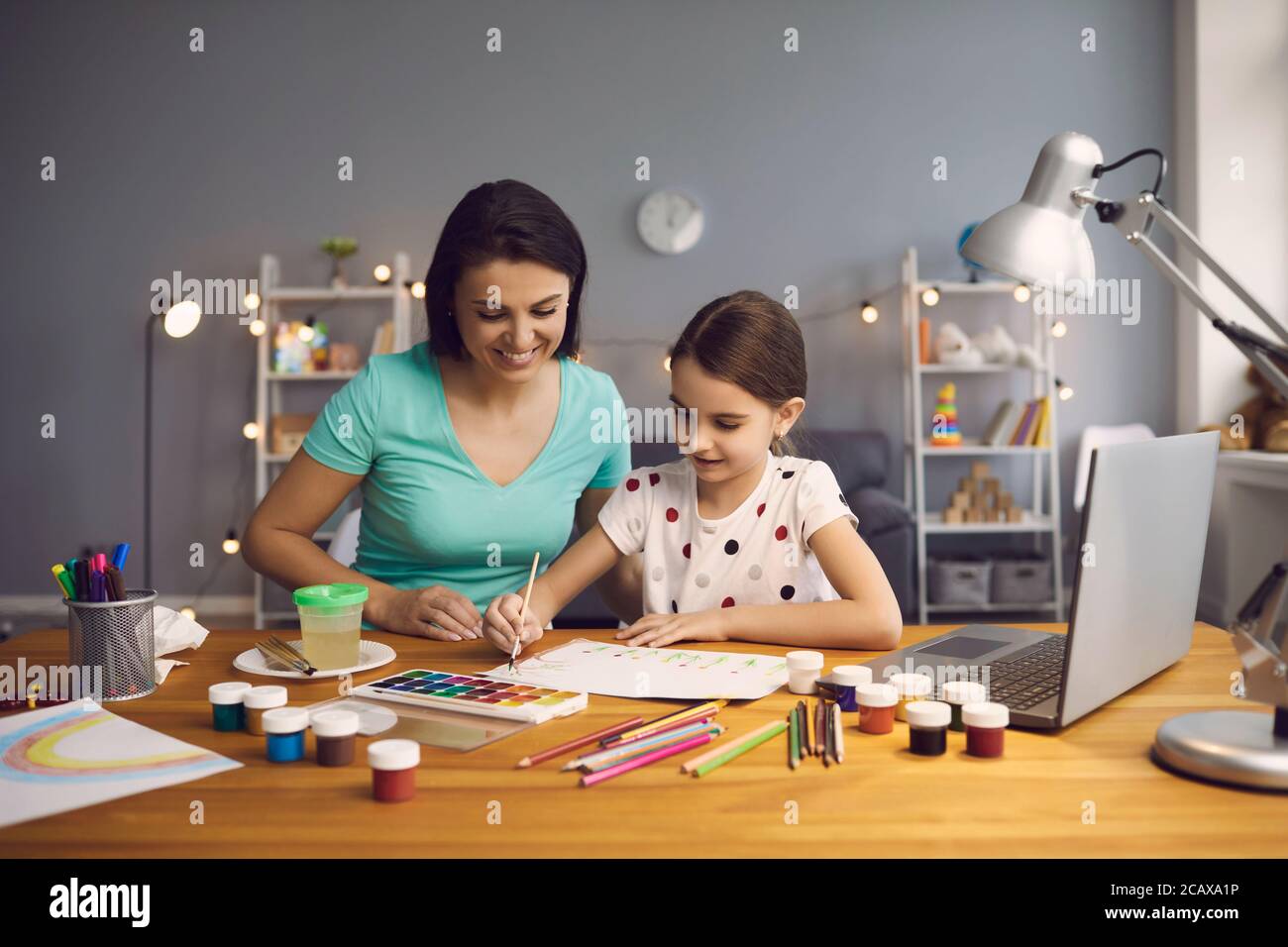 Kleines Mädchen nimmt Online-Kunstunterricht mit Mutter hilft ihr zu Hause. Kind und Eltern Zeichnung zusammen zu Video-Tutorial auf Laptop Stockfoto