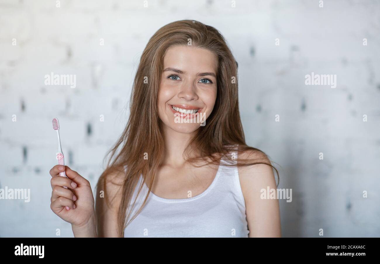 Portrait von schönen Frau mit strahlendem Lächeln hält Zahnbürste drinnen Stockfoto