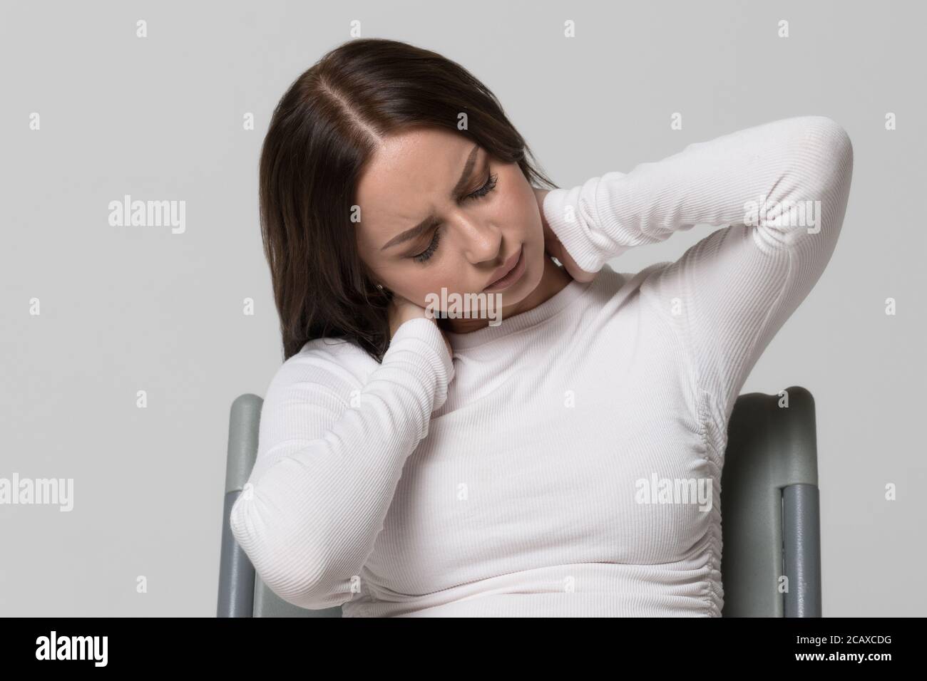Nahaufnahme Porträt einer ungesunden Frau in weiß oben mit Schmerzen in ihrem Hals und Rücken. Halsarthritis, Osteochondrose, Erkrankungen des Bewegungsapparates Stockfoto