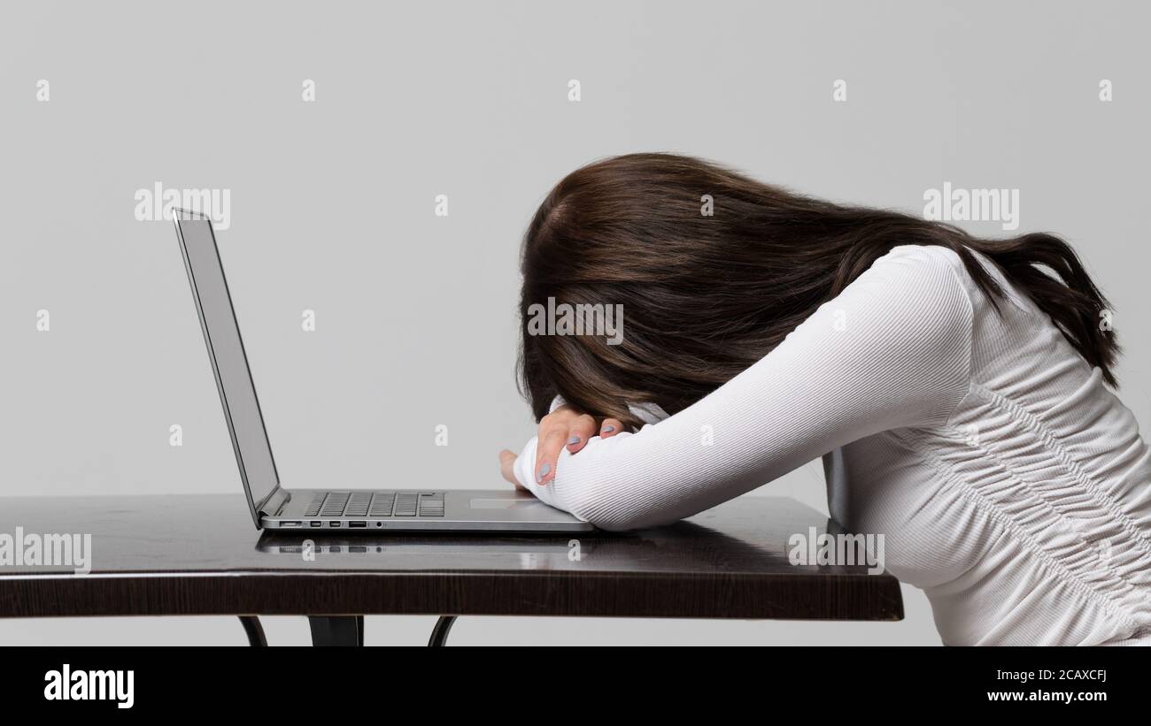 Müdigkeit, Kopfschmerzen, Überanstrengung. Frau schlief ein, nachdem sie an seinem Laptop gearbeitet hatte, Seitenansicht, isoliert auf grauem Hintergrund. Schlaf, Überstunden, Büro wo Stockfoto