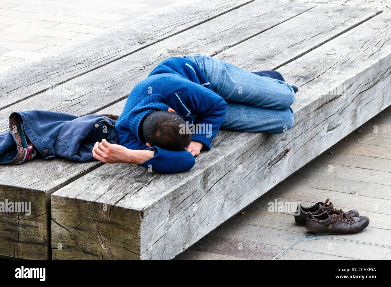 Ein junger Mann, der ein Mittagsschlaf auf einer Holzbank in King's Cross, London, Großbritannien, macht Stockfoto