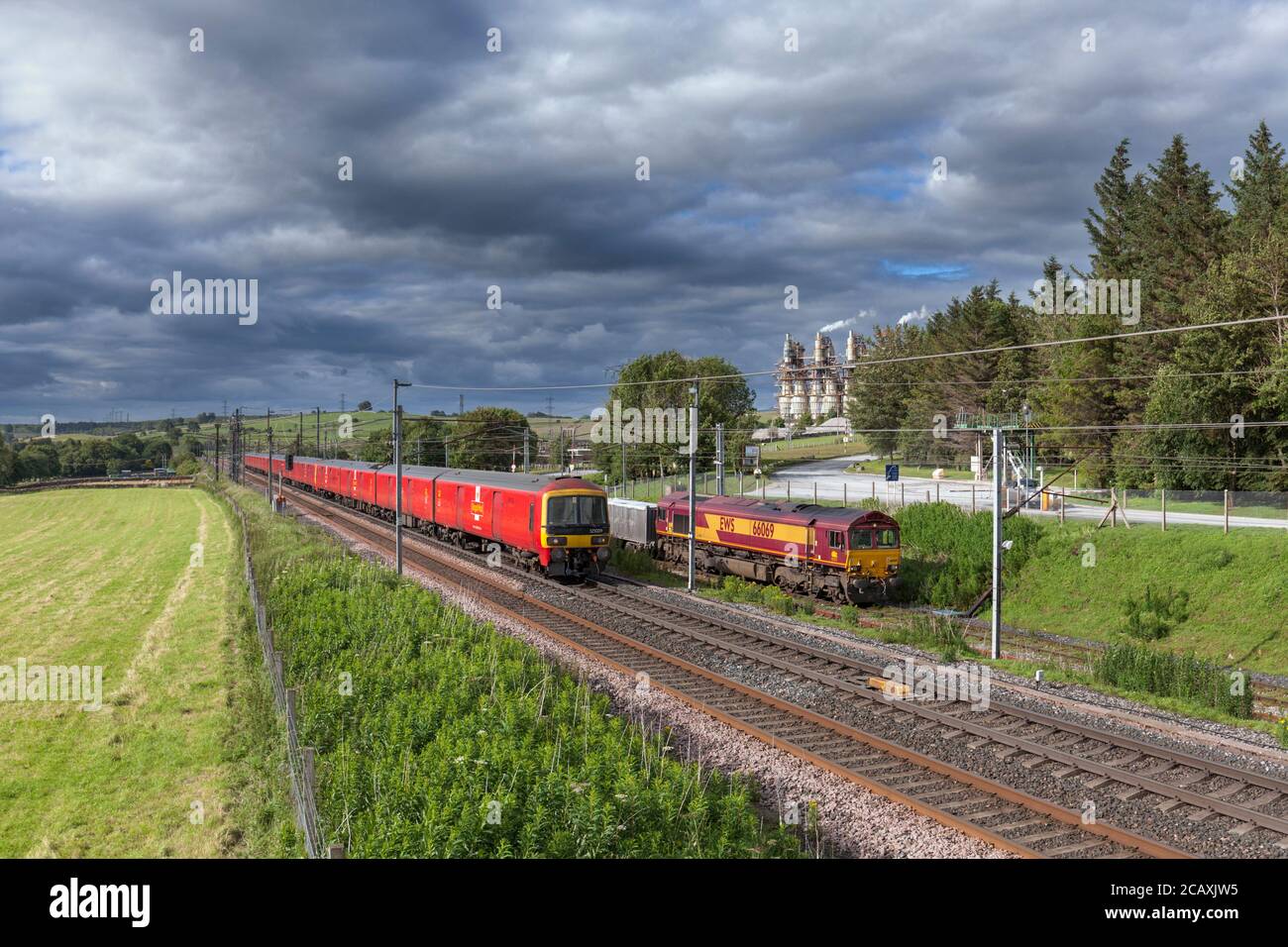 Royal Mail Klasse 325 vorbei an einer DB Cargo Klasse 66 Lokomotive mit Güterzug bei Hardendale Kalk arbeitet weiter Die Hauptlinie der Westküste in Cumbria Stockfoto