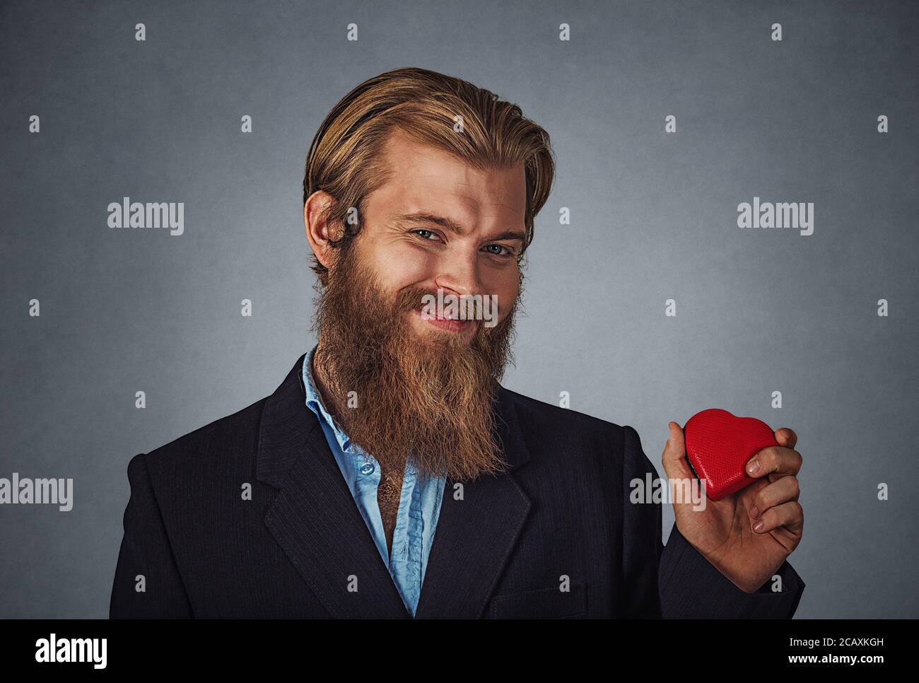 Junge glücklich Kaukasischen bärtigen hipster Geschäftsmann halten roten herzförmigen Geschenkbox für Valentinstag bereit. Auf Grau Grau studio Wand Hinterg isoliert Stockfoto