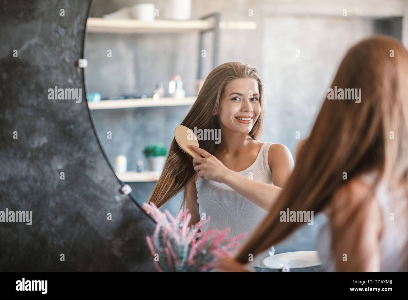 Junge Frau putzt ihre schönen langen Haare mit Holzbürste in der Nähe Spiegel drinnen, kopieren Raum Stockfoto
