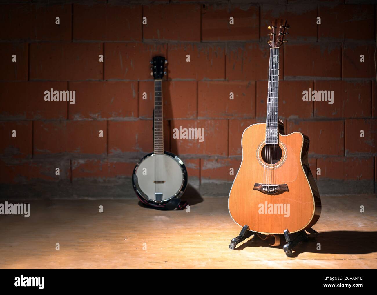 Akustische Gitarre und ein verschwommenes Banjo der Hintergrund vor einer rohen Backsteinwand im Proberaum einer Garagenband, Kopierraum, ausgewählter Fokus, schmal Stockfoto