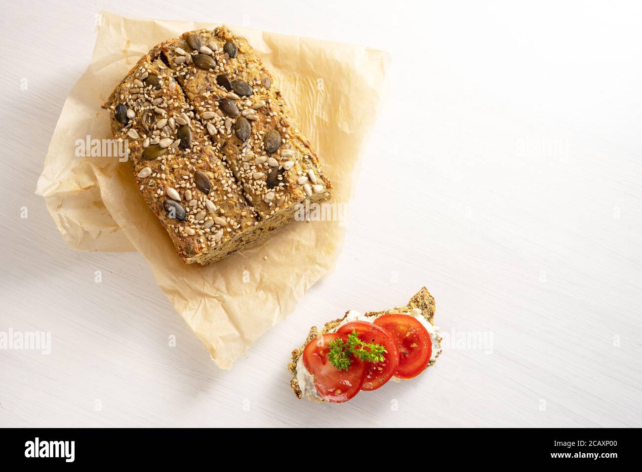 Kohlenhydratarmes Eiweißbrot mit Samen auf Backpapier und Tomatenbrot mit Petersilie garnieren auf einem weißen Tisch, gesunde Schlankheitskost, Kopierraum hoch Stockfoto
