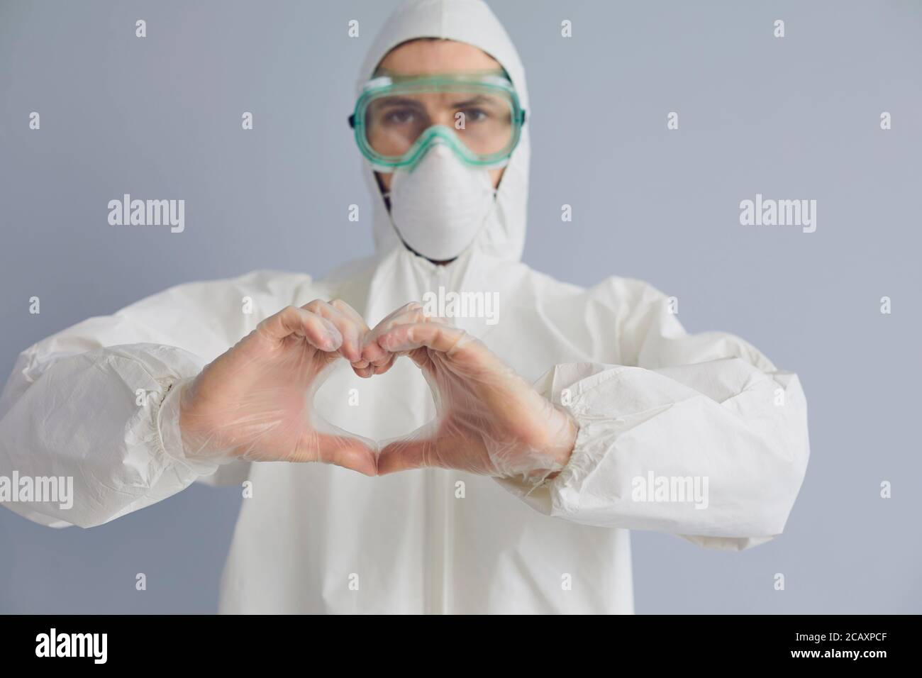 Doktor in Hazmat Anzug zeigt Herz mit Händen auf grauem Hintergrund. Medic Förderung der Spende zur Bekämpfung der Epidemie Stockfoto