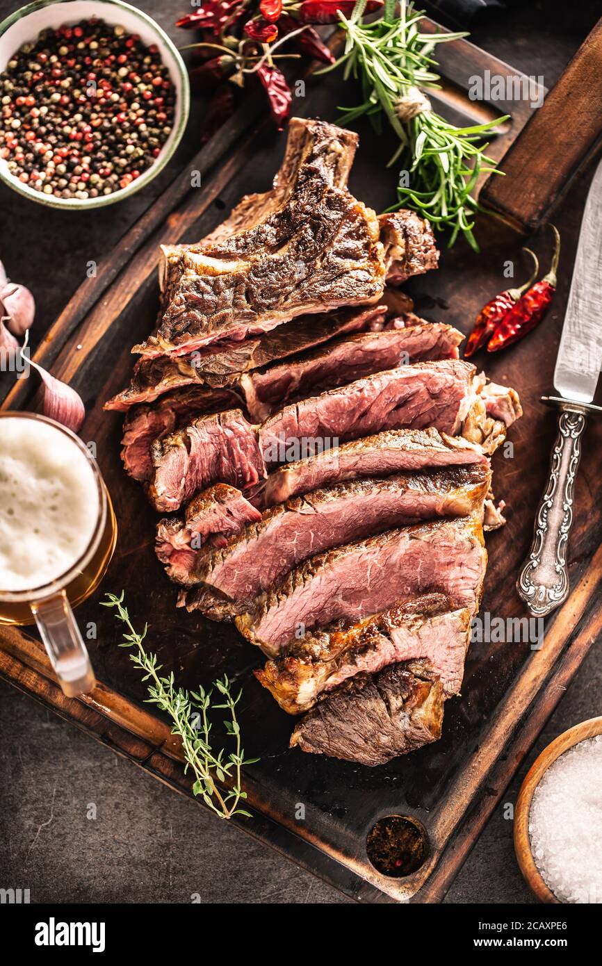 Scheiben von saftigem Rindfleisch Steak Gabel Messer Gewürze Salz Pfeffer Kräuter und Bier vom Fass Stockfoto