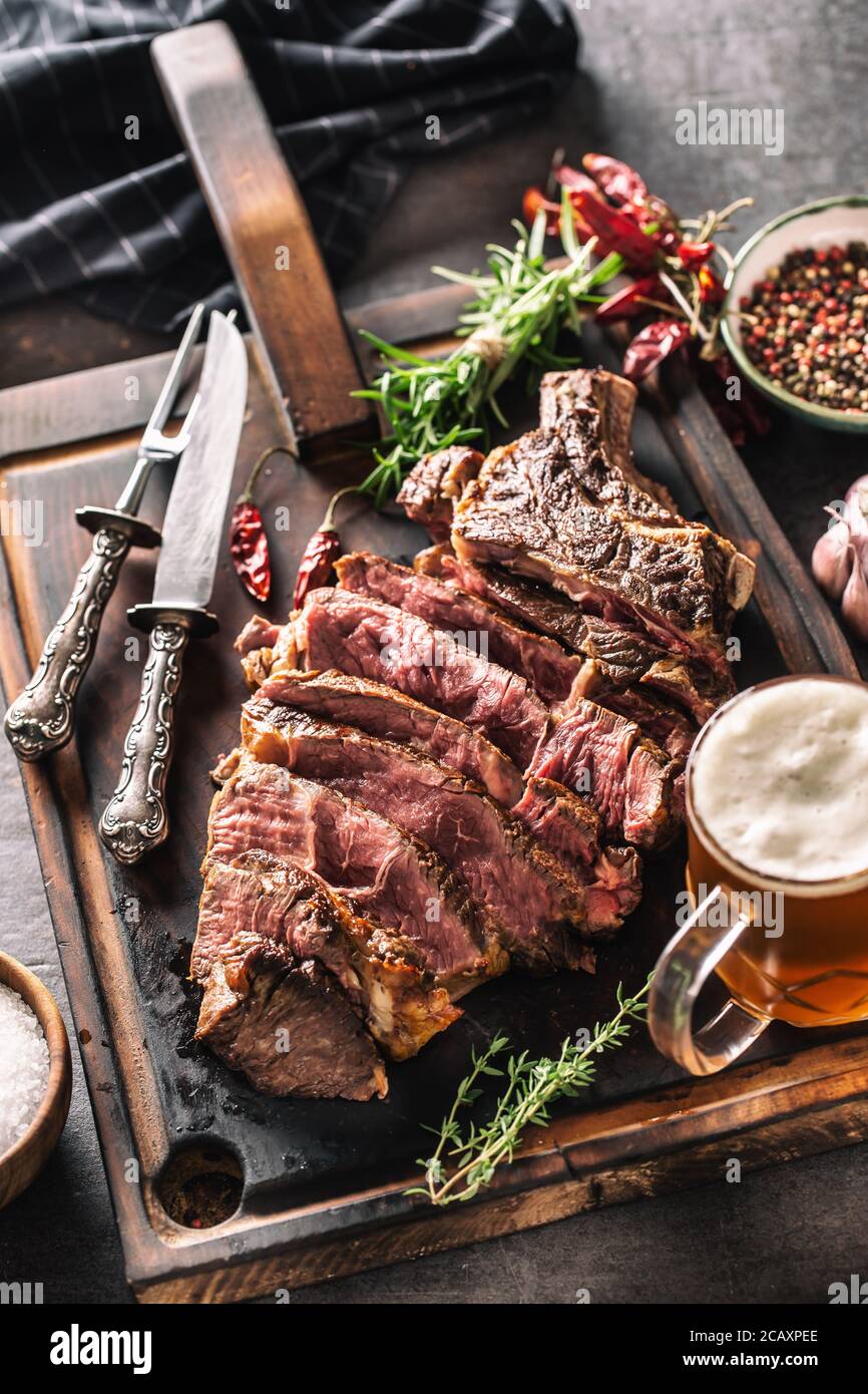 Scheiben von saftigem Rindfleisch Steak Gabel Messer Gewürze Salz Pfeffer Kräuter und Bier vom Fass Stockfoto