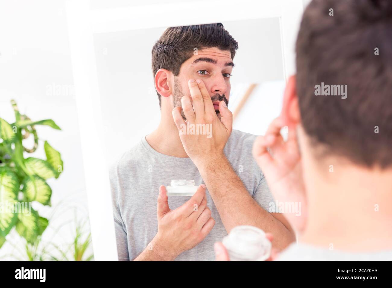 Schuss von gutaussehenden Mann Anwendung Hautpflege Gesichtsbehandlung Creme auf Gesicht im Badezimmer, während vor dem Spiegel stehen. Stockfoto