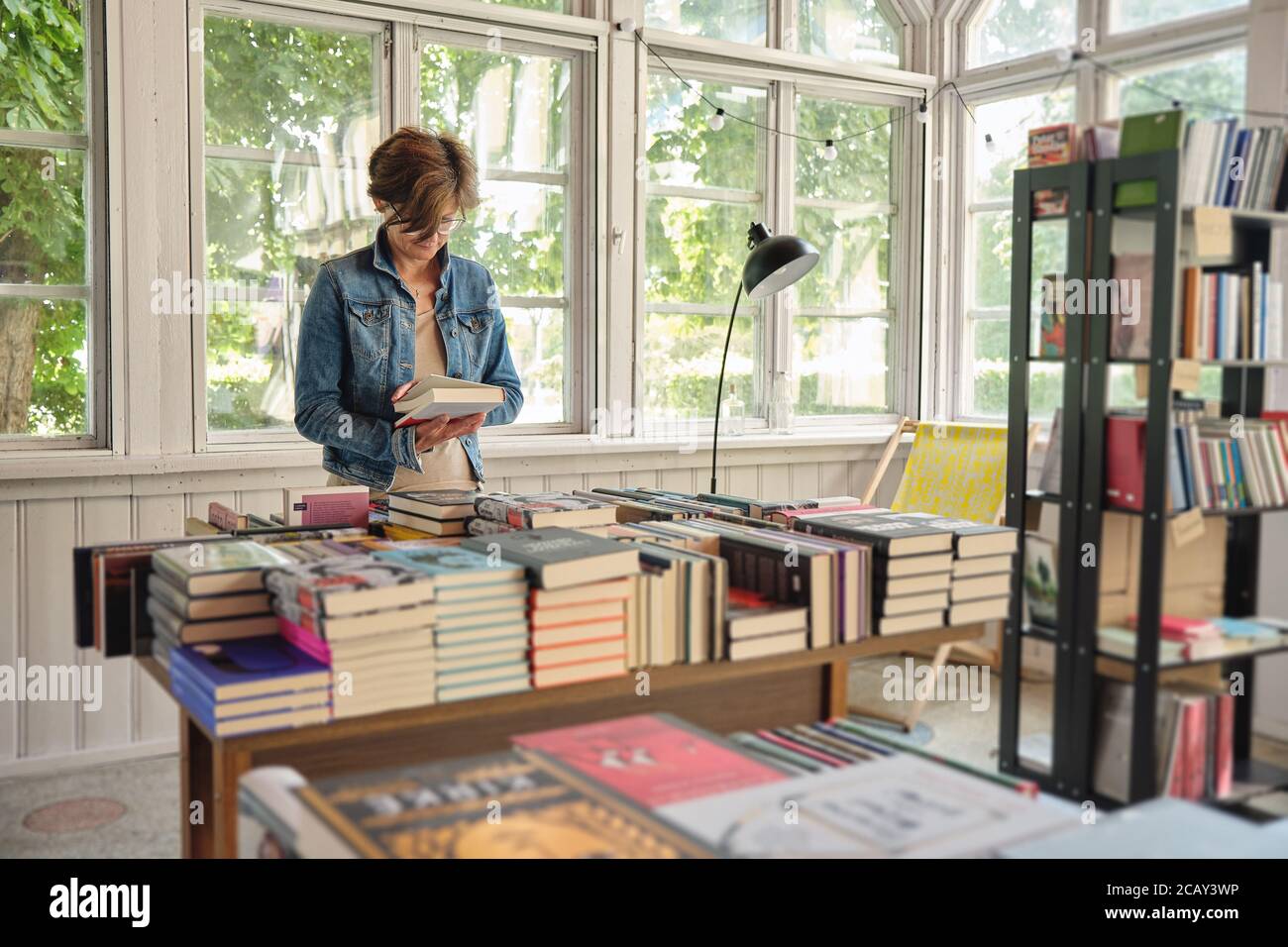Einsame kaukasische Frau mittleren Alters, die ein Buch im Vintage liest Buchhandlung Stockfoto