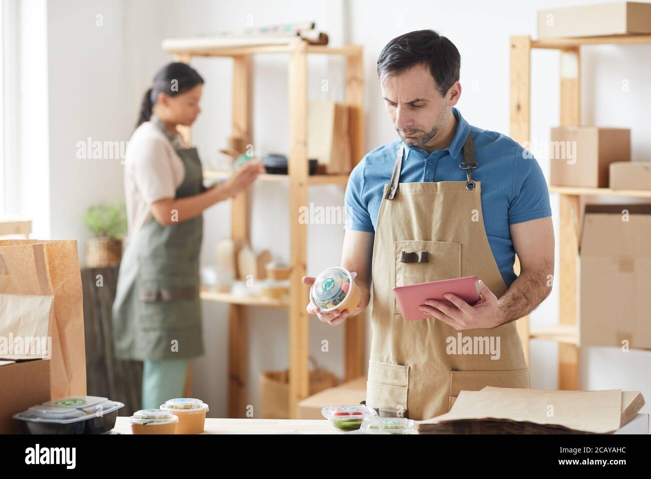 Waist up Porträt von reifen Arbeiter trägt Schürze Verpackungsaufträge, während Sie am Holztisch stehen, Lebensmittel-Lieferservice, Kopierer Platz Stockfoto