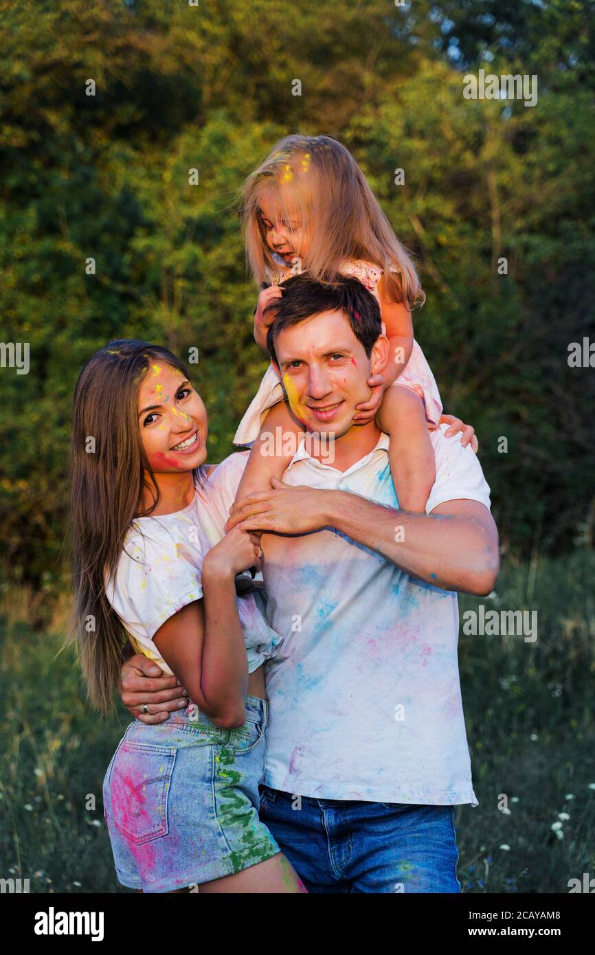 Schöne Familie, Mama, Papa und Tochter spielen mit Holly Farben.  Mehrfarbige Farbe auf Kleidung und Gesicht Stockfotografie - Alamy