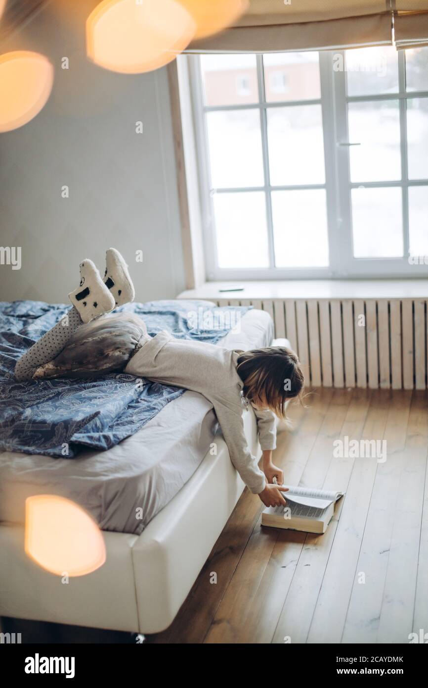 Kleines nettes Mädchen hält ein Buch auf dem Boden und dreht seine Seiten. Seitenansicht Foto. Stockfoto